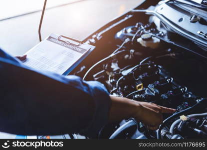 Car mechanic holding clipboard and checking to maintenance vehicle by customer insurance claim order in auto repair shop garage. Engine repair service. People occupation and business job. technician