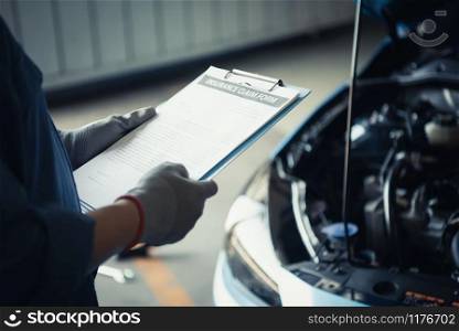Car mechanic holding clipboard and checking to maintenance vehicle by customer insurance claim order in auto repair shop garage. Engine repair service. People occupation and business job. technician