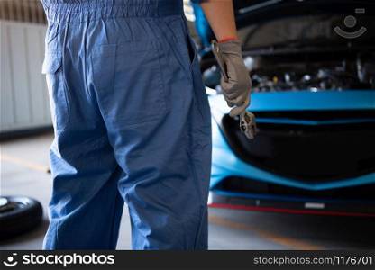 Car mechanic holding wrench for fixing to customer claim order in a auto repair garage workshop. Engine repair service. People occupation and business job. Automobile industry technical maintenance