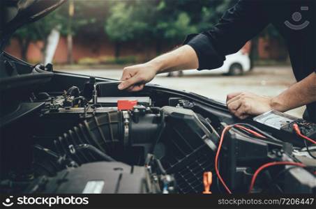 Car mechanic is checking the engine and holding the battery gauge.