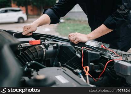 Car mechanic is checking the engine and holding the battery gauge.