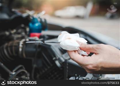 Car mechanic is checking the engine oil of the car using a steel and cleaner by tissue.
