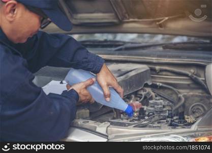 Car Mechanic man hands pouring Deionized purified Distilled water for car battery mechanical service. Close up hands man hold Deionized Distilled liquid water bottle at garage auto mobile car service