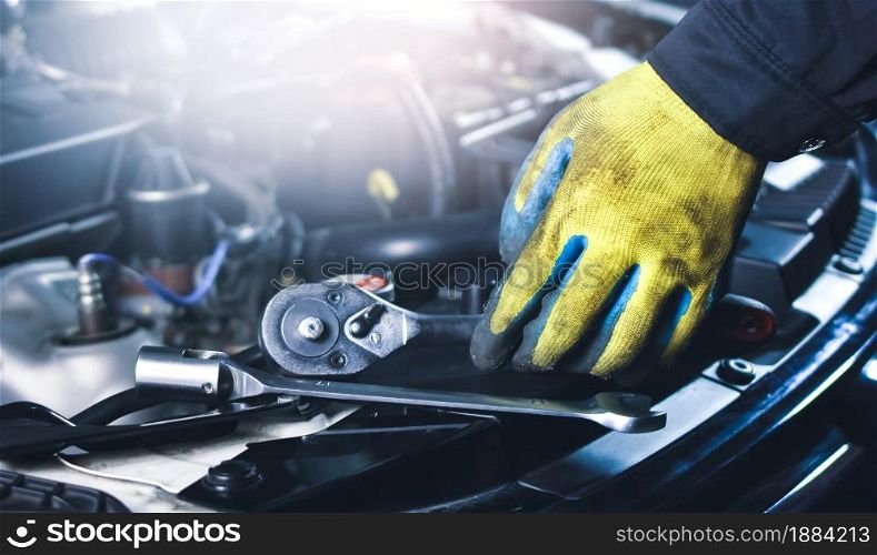 Car mechanic picking up socket wrench and tools on the car body in the repair garage