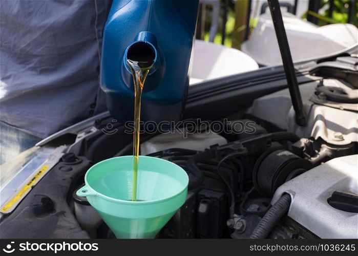 Car mechanic replacing and pouring fresh oil into engine at maintenance repair