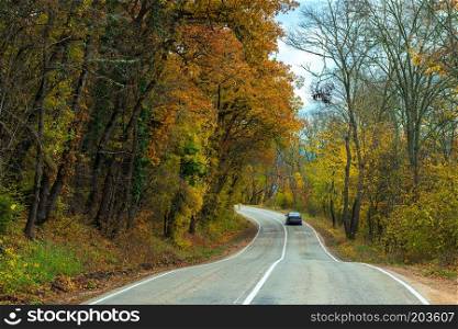 Car moving along a winding road in the mountains on an autumn afternoon