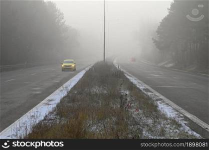 Car on the road in the fog. Autumn landscape - dangerous road traffic in winter season.