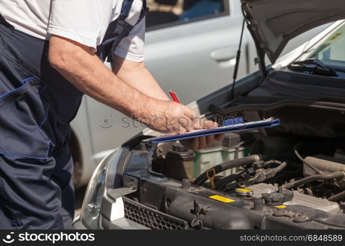 Car or motor mechanic checking a car engine and writing on the clipboard. Auto mechanic checking car engine and writing on the clipboard
