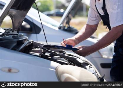 Car or motor mechanic checking a car engine and writing on the clipboard. Auto mechanic checking car engine and writing on the clipboard