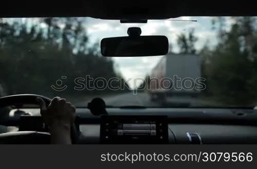 Car overtaking truck on motorway in the forest. View from inside of vehicle&acute;s interior. Woman driving car on high speed motorway and overtaking lorry during summer road trip.