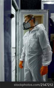Car painter wearing protective mask, gloves and clothes entering painting booth chamber workshop. Car painter in protective clothes entering booth