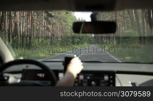 Car riding on rural road that runs through the forest. View form inside of auto. Woman driving empty country road in the wood and using gps navigation on smartphone.