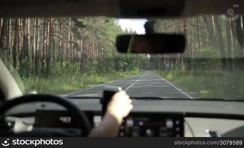 Car riding on rural road that runs through the forest. View form inside of auto. Woman driving empty country road in the wood and using gps navigation on smartphone.