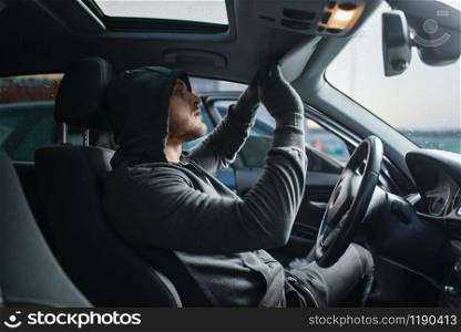 Car robber searches the interior, dangerous hobby, stealing. Hooded male bandit opening vehicle on parking. Auto robbery, automobile crime