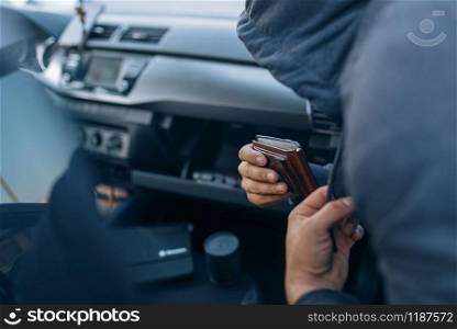 Car robber takes the wallet from the glove compartment, criminal lifestyle, stealing. Hooded male bandit opening vehicle on parking. Auto robbery, automobile crime. Car robber takes the wallet, stealing