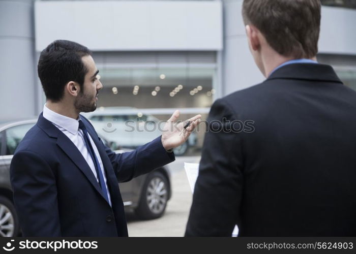 Car salesman holding car keys and selling a car to a young businessman