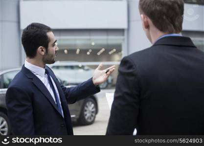 Car salesman holding car keys and selling a car to a young businessman