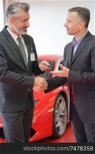 Car salesman shaking hands with customer and passing keys