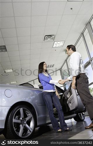 Car salesman shaking hands with female customer in showroom