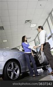Car salesman shaking hands with female customer in showroom