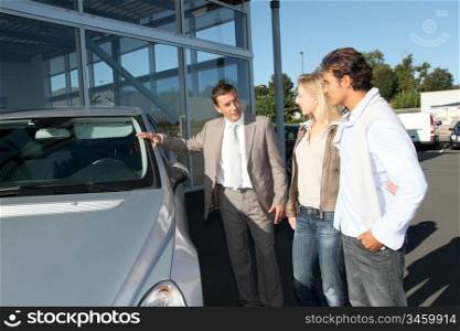 Car seller showing vehicle to couple of purchasers