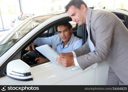 Car seller with car buyer looking at electronic tablet