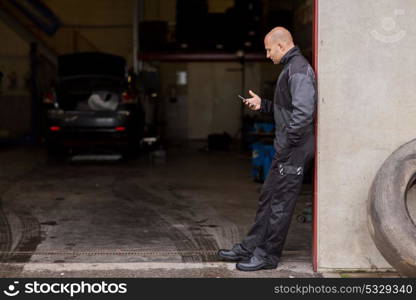 car service and people concept - auto mechanic with smartphone at break outdoor. auto mechanic with smartphone at car service