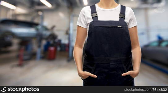 car service, job and profession concept - close up of female worker in overall over auto repair shop on background. close up of female worker at car service