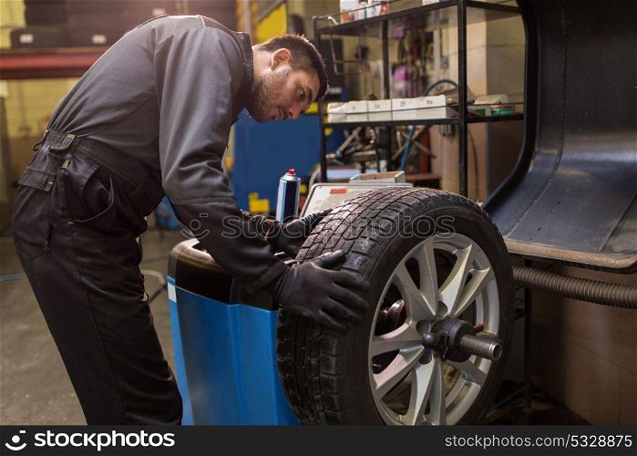 car service, repair, maintenance and people concept - auto mechanic man balancing tire at workshop. auto mechanic balancing car tire at workshop
