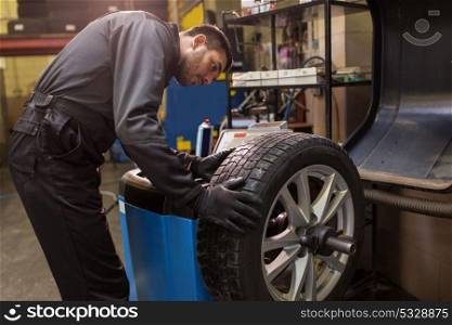 car service, repair, maintenance and people concept - auto mechanic man balancing tire at workshop. auto mechanic balancing car tire at workshop