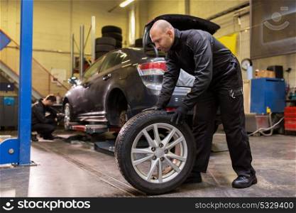 car service, repair, maintenance and people concept - auto mechanic man changing tire at workshop. auto mechanic changing car tire at workshop