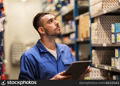 car service, repair, maintenance and people concept - auto mechanic man or smith with tablet pc computer looking for spares at workshop or warehouse
