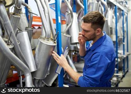 car service, repair, maintenance and people concept - auto mechanic man or smith with clipboard and mufflers calling on phone at workshop warehouse