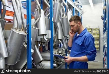car service, repair, maintenance and people concept - auto mechanic man or smith with clipboard and mufflers calling on phone at workshop warehouse