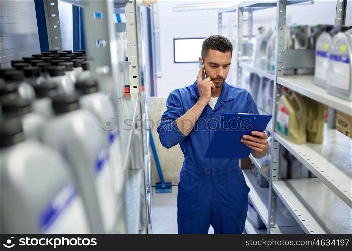 car service, repair, maintenance and people concept - auto mechanic man or smith with clipboard calling on smartphone at workshop or warehouse