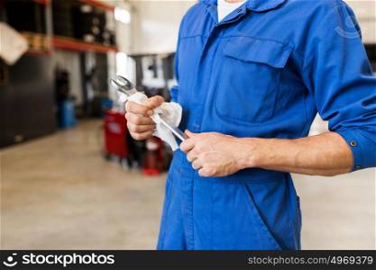 car service, repair, maintenance and people concept - auto mechanic man or smith with wrench at workshop. auto mechanic or smith with wrench at car workshop