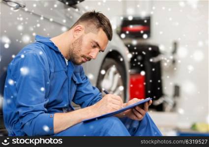 car service, repair, maintenance and people concept - auto mechanic man or smith with clipboard writing at workshop over snow. auto mechanic man with clipboard at car workshop