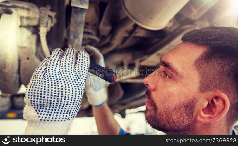 car service, repair, maintenance and people concept - auto mechanic man or smith with flashlight working at workshop. mechanic man with flashlight repairing car at shop