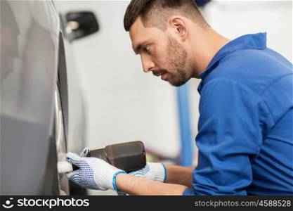 car service, repair, maintenance and people concept - auto mechanic man with electric screwdriver changing tire at workshop