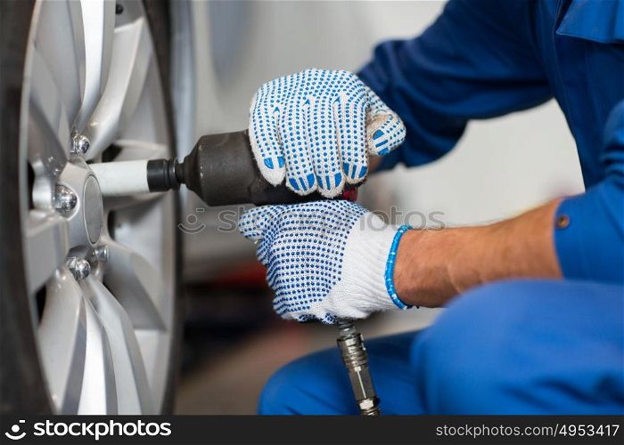 car service, repair, maintenance and people concept - auto mechanic man with screwdriver changing tire at workshop. mechanic with screwdriver changing car tire