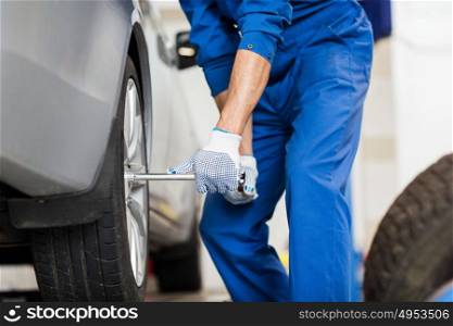 car service, repair, maintenance and people concept - auto mechanic man with electric screwdriver changing tire at workshop. mechanic with screwdriver changing car tire