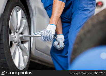 car service, repair, maintenance and people concept - auto mechanic man with electric screwdriver changing tire at workshop. mechanic with screwdriver changing car tire