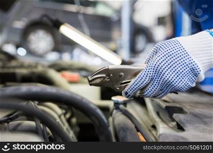 car service, repair, maintenance and people concept - auto mechanic man with lamp and pliers working at workshop. mechanic man with pliers repairing car at workshop