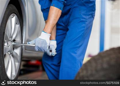 car service, repair, maintenance and people concept - auto mechanic man with electric screwdriver changing tire at workshop. mechanic with screwdriver changing car tire