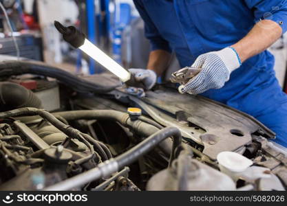 car service, repair, maintenance and people concept - auto mechanic man with lamp and pliers working at workshop. mechanic man with pliers repairing car at workshop