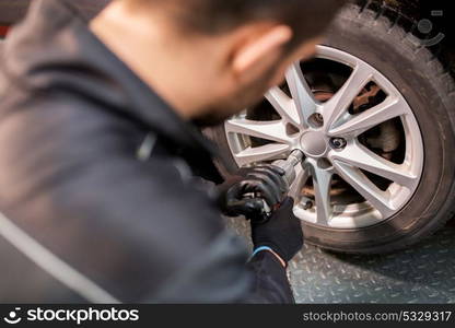 car service, repair, maintenance and people concept - auto mechanic man with electric screwdriver changing tire at workshop. auto mechanic with screwdriver changing car tire