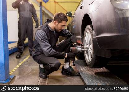 car service, repair, maintenance and people concept - auto mechanic man with electric screwdriver changing tire at workshop. auto mechanic with screwdriver changing car tire