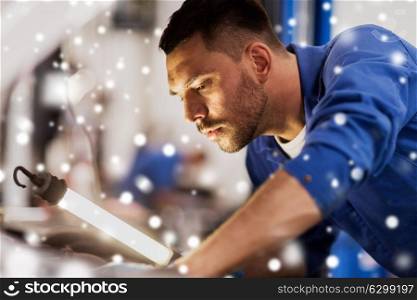 car service, repair, maintenance and people concept - auto mechanic man with lamp working at workshop over snow. mechanic man with lamp repairing car at workshop