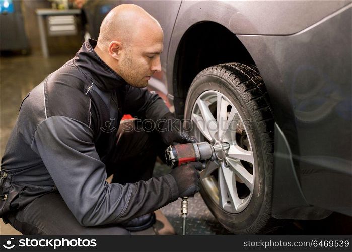 car service, repair, maintenance and people concept - auto mechanic man with electric screwdriver changing tire at workshop. auto mechanic with screwdriver changing car tire