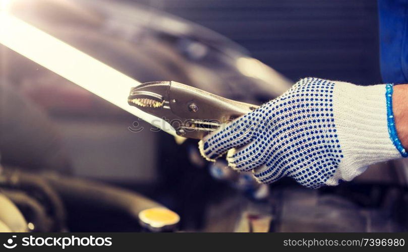 car service, repair, maintenance and people concept - auto mechanic man with lamp and pliers working at workshop. mechanic man with pliers repairing car at workshop